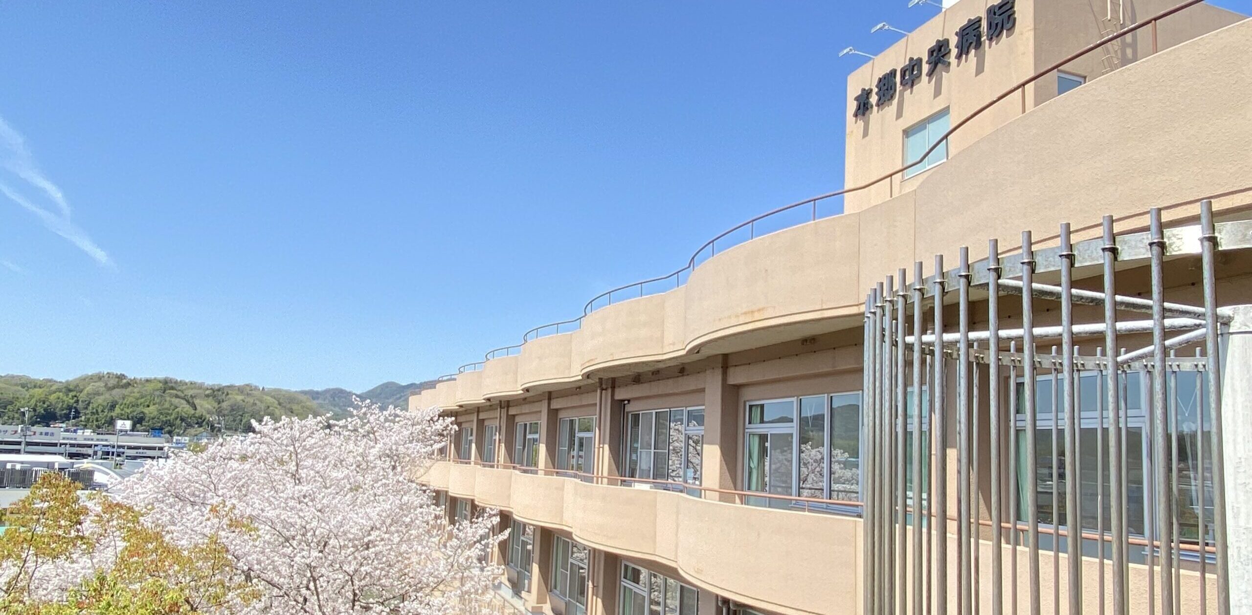 病院の外観写真。青空の下、中庭に咲いた桜が病院の窓に映って見えます。